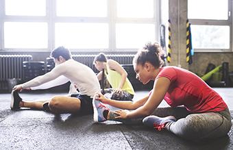 Three young adults stretching indoors at a gym